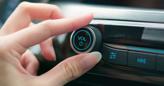 auto audio concept - close up of woman turning on radio knob button and adjust music sound volume in car