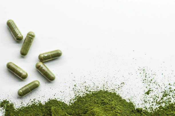 grünes pulver mit grünen kapseln auf weißem hintergrund. - vitamin pill nutritional supplement capsule antioxidant stock-fotos und bilder