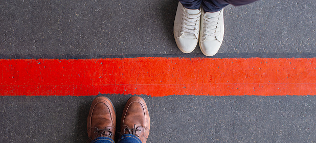 Quarantine, social distancing and differences concept. Man and woman standing opposite of each other, divided by a thick red line. Wide angle view, copy space.