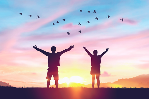 Couple rising hands and birds flying on sunset sky at nature field abstract background. Freedom feel good and travel adventure concept. Vintage tone filter effect color style.
