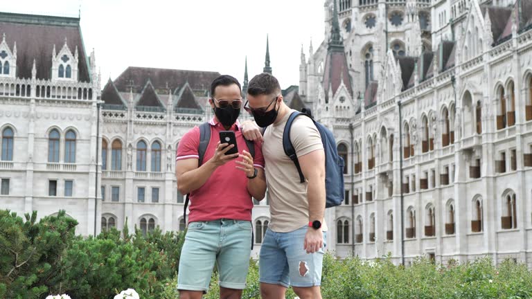 Gay tourists with face masks, photographing each other near famous building - normal speed video