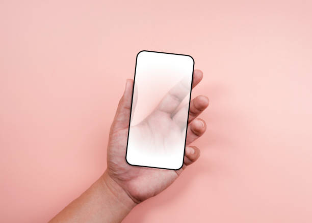 istock Hand holding smartphone with a white blank screen with black frame isolated on pastel pink background. Mockup transparent future phone in hand, minimal style. 1363568530