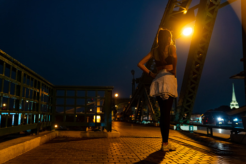 Confidence Hispanic woman in sportswear jogging on the bridge in the city at night. Healthy wellness female athlete enjoy outdoor lifestyle sport training workout fitness exercise and running