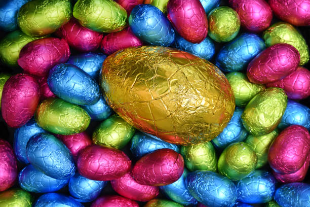 istock Pile or group of multi colored and different sizes of colourful foil wrapped chocolate easter eggs in pink, blue, yellow and lime green with a large gold egg in the middle. 1363573659
