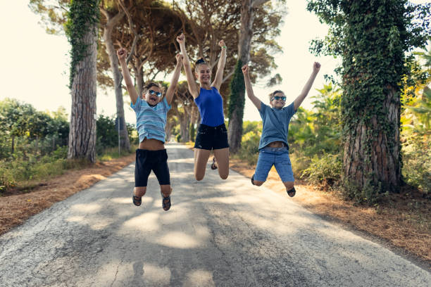 Three kids hiking in Tuscany, Italy. Kids are jumping with joy on the road.\nCanon R5