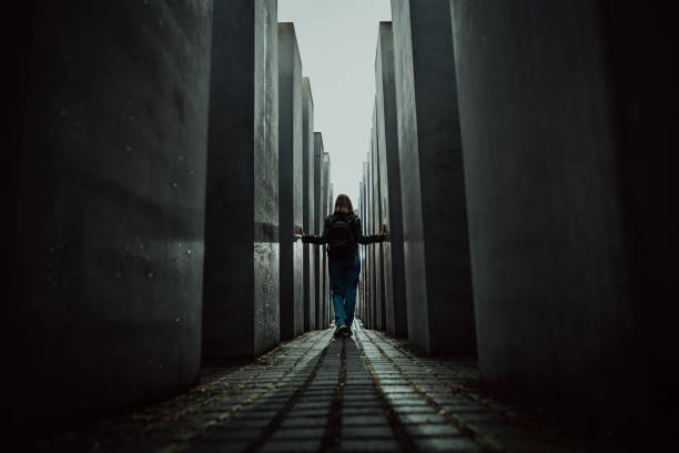 ottobre 2021 - berlino, germania. la donna si trova in un labirinto buio tra alti blocchi nel memoriale ebraico dell'olocausto degli ebrei assassinati. luce alla fine del tunnel. - anti semitism foto e immagini stock