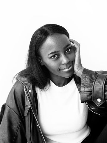 Close up portrait of beautiful black african american girl with neutral make-up wearing white top and black faux leather jacket. Smiling ,looks fresh and lovely Fashion model studio portrait on white background Perfect glowing skin Beauty Fitness Healthcare concept Black and white photo