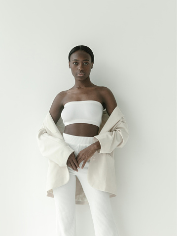 Full length portrait of young woman with afro hairstyle wearing white sweater and pants, looking at camera.