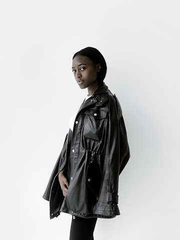 Waist up portrait of beautiful black african american girl with neutral make-up wearing white top and black faux leather jacket and black pants. Looks fresh and lovely Fashion model studio portrait on white background Perfect glowing skin Beauty Fitness Healthcare concept