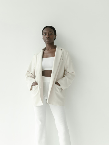 Waist up portrait of beautiful black african american girl with neutral make-up wearing white crop top jacket and pants. Looks fresh and lovely Fashion model studio portrait on white background Perfect glowing skin Beauty Fitness Healthcare concept