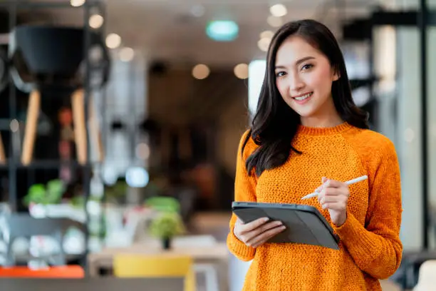 Photo of smart confidence asian female startup entrepreneur small business owner businesswoman wear smart casual cloth smile hand use tablet woking inventory checking in showroom office daytime background