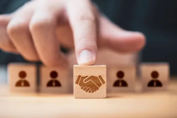 Photo of Hand putting hand shaking which print screen on wooden cube block  in front of human icon for business deal and agreement concept.