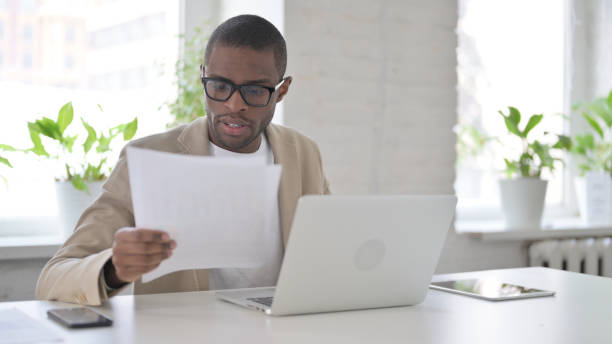 istock African Man with Laptop Reading Documents in Office 1363583998