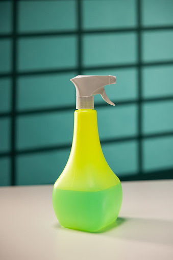 Green plastic spray bottle on the table in front of a teal background with shadow from window slats
