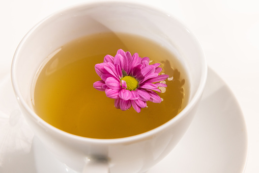 High angle view close up of ceramic cup of tea with pink flower float inside