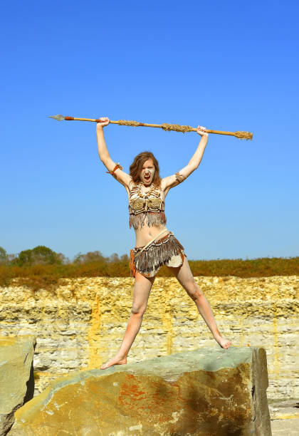 A young woman is dressed as Stone Age warrior. Her body and face is covered with mud and dirt.She is seen posing in a stone quarry.
