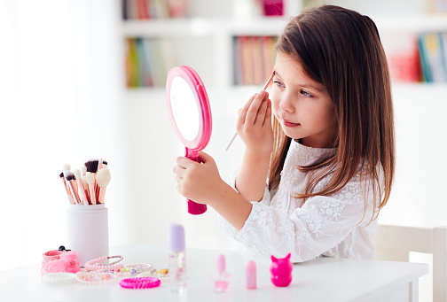 beautiful young girl, kid applying makeup with brush and pocket mirror