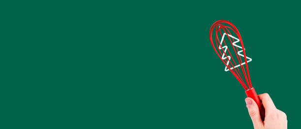 Red whisk tool in hand over green background. Whipping beater with Christmas tree inside. Banner with copy space for text.
