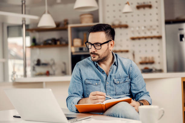 istock A focused man writing down tasks and looking at the laptop at his cozy home. 1363590358
