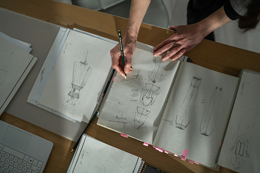 Female atelier sitting at table in studio and drawing new fashion models