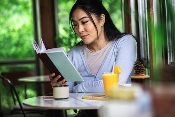istock Young Asian woman sitting in cafe reading a book. 1363592592
