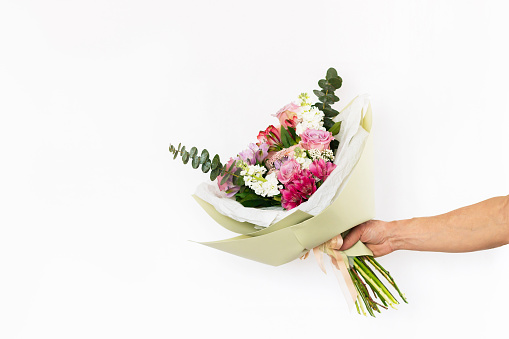 Bouquet of flowers in a stylish festive package in a male hand isolated on a white background. Colorful pink and orange roses, spring. A gift for the 8th of March. Copy space for text or design