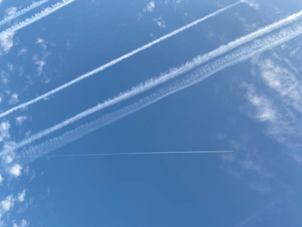 istock Airplane in the blue sky with clouds from below. High flying passenger plane with condensation trail. Jets flying overhead diagonally in sky with sunlight. Bottom view 1363593720