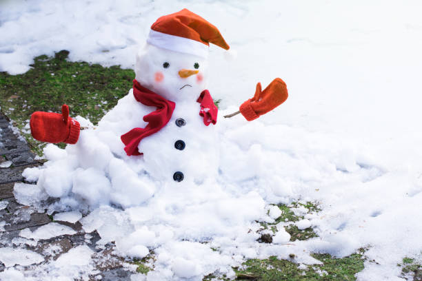 infeliz muñeco de nieve con mitones, bufanda roja y gorra se está derritiendo al aire libre a la luz del sol - melting snowman winter spring fotografías e imágenes de stock