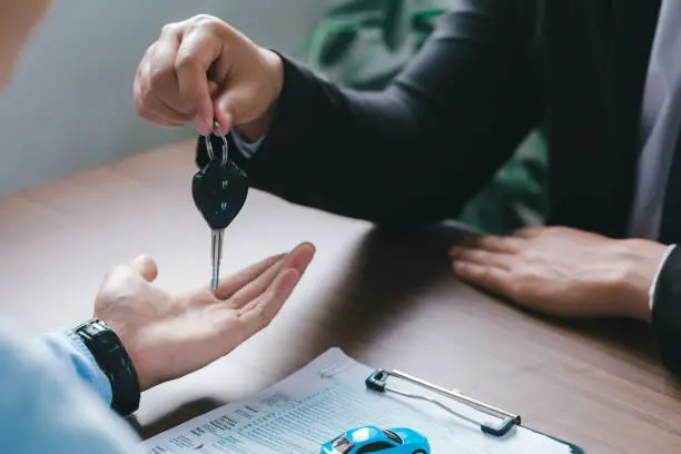 Photo of Close up view Hand of car salesman giving car key to the customers after who signed the purchase contract legally, Successful completion of car sales, Purchase contract,