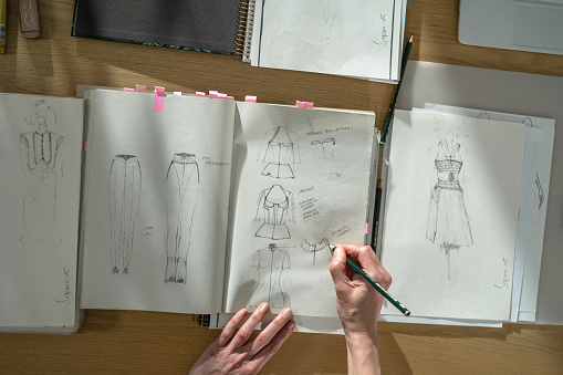 Female atelier sitting at table in studio and drawing new fashion models