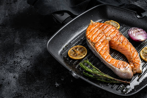 istock Salmon Fish Steak grilled on a grill pan with herbs. Black background. Top view. Copy space 1363599188