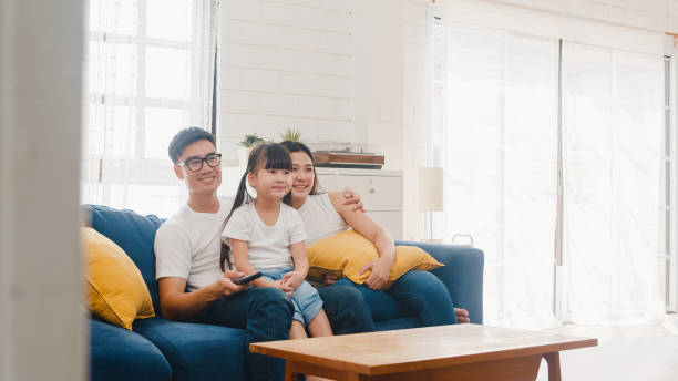 feliz familia asiática disfrutar de su tiempo libre relajarse juntos en casa. estilo de vida coreano papá, mamá e hija viendo la televisión juntos y divirtiéndose acostado en el sofá en la sala de estar en la casa moderna. - apartment television family couple fotografías e imágenes de stock