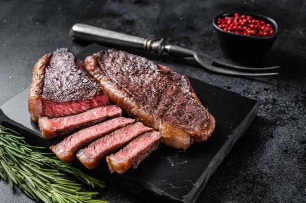 Grilled top sirloin or cup rump beef meat steak on marble board. Black background. Top view.