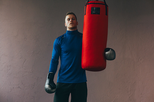 Serious man standing tired after exercising with a punching bag and looking at camera.