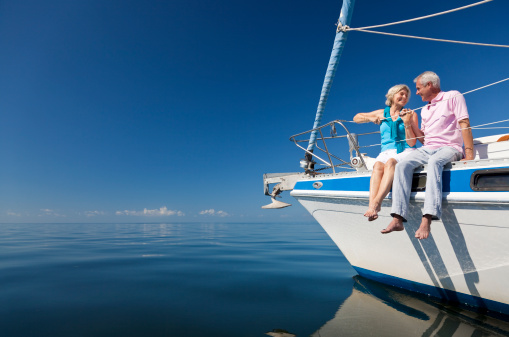 A happy senior couple sitting on the front of a sail boat on a calm blue sea