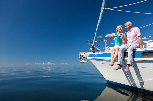 Happy Senior Couple on the Bow of a Sail Boat A happy senior couple sitting on the front of a sail boat on a calm blue sea sailing couple stock pictures, royalty-free photos & images