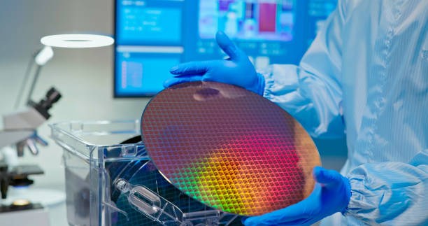 technician with wafer close up of asian male technician in sterile coverall holds wafer that reflects many different colors with gloves and check it at semiconductor manufacturing plant computer wafer stock pictures, royalty-free photos & images