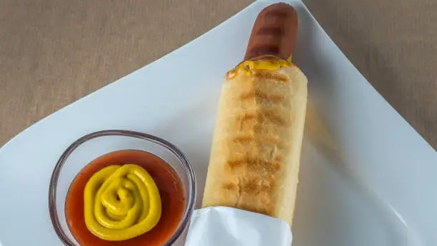 Photo of Appetizing French Hot Dog on white plate. Sausage in a bun with ketchup and mustard.