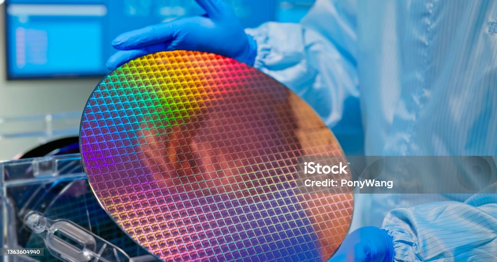technician with wafer close up of asian male technician in sterile coverall holds wafer that reflects many different colors with gloves and check it at semiconductor manufacturing plant Semiconductor Stock Photo