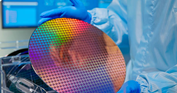 technician with wafer close up of asian male technician in sterile coverall holds wafer that reflects many different colors with gloves and check it at semiconductor manufacturing plant computer wafer stock pictures, royalty-free photos & images