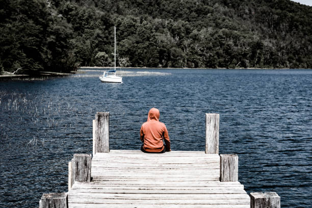 Young man sitting peacefully on the tip of a pier. Looking at the beauty around him
