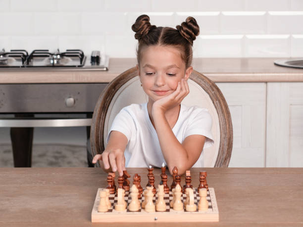 la niña está jugando al ajedrez en casa. hace el primer movimiento. - concentration chess playing playful fotografías e imágenes de stock