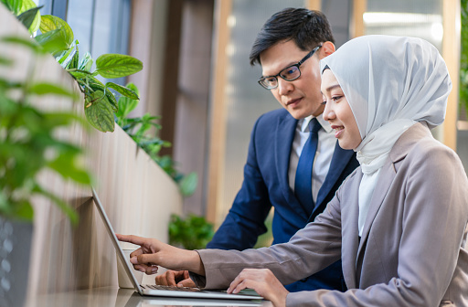 Young Muslim businesswoman with businessman looking at laptop together while working at the workplace
