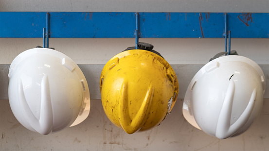 Yellow and white safety helmet which is keep at metal rail rack at the factory wall, Industrial PPE object photo.