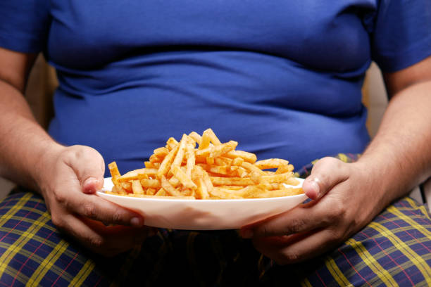 a fat man eating french fries while sited a fat man eating french fries while sited . big plate of food stock pictures, royalty-free photos & images