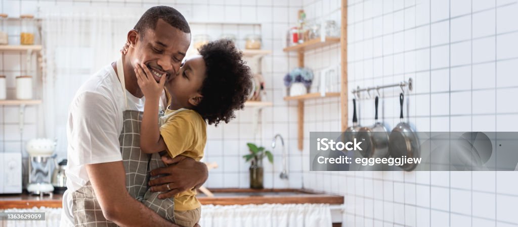 Happy African American father and his son at kitchen, Loving Black little Boy embracing and kiss his Dad, Banner, Panoramic Portrait of Happy African American father and his son while cooking at kitchen, Loving Black little Boy embracing and kiss his Dad, Banner, Panoramic Father Stock Photo