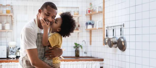 szczęśliwy afroamerykański ojciec i jego syn w kuchni, kochający czarny mały chłopiec obejmujący i całujący swojego tatę, banner, panoramiczny - mature adult male men portrait zdjęcia i obrazy z banku zdjęć
