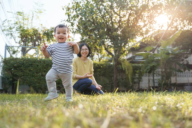 retrato de un niño asiático sonriente y su joven madre en la naturaleza con la luz del sol, feliz hogar familiar. - baby mother summer park fotografías e imágenes de stock