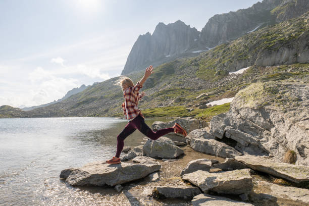 l'escursionista femmina salta da una roccia all'altra sopra il lago alpino - european alps women summer outdoor pursuit foto e immagini stock
