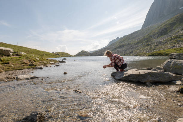 istock Young woman scooping water from alpine lake 1363630616